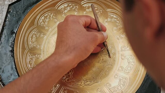 Master, tinsmith, creates a pattern on a brass dish or tray. Close-up. Copper master, hands detail of craftsman at work. Uzbekistan, Bukhara.