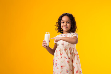 Smiling child girl holding glass of milk and pointing finger at it. Nutrition and health concept