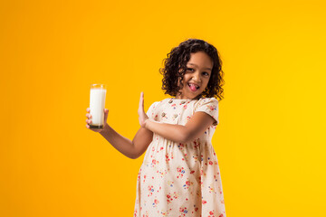 Kid girl with dairy allergy holding glass of milk on yellow background. Lactose intolerance concept - obrazy, fototapety, plakaty