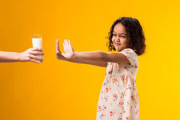Kid girl with dairy allergy holding glass of milk on yellow background. Lactose intolerance concept