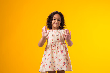 Child girl showing stop gesture on yellow background. Bulling and negative emotions concept