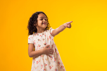 Kid girl mocking and teasing at someone showing finger at camera and holding stomach over yellow background. Bulling concept