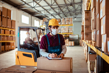 Warehouse worker with facemask checking inventory in storage aisle