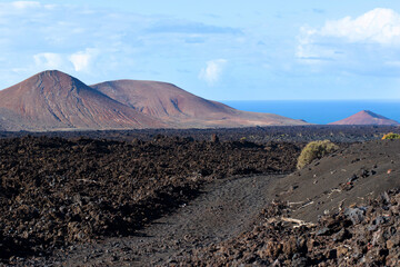 Black lava field and colorful mountains on hiking Termesana route (Ruta de Termesana) in Timanfaya national park, Lanzarote, Canary Islands , Spain