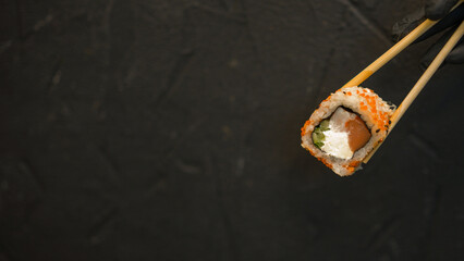 Sushi rolls on a dark background. The hand holds the roll. Sushi sticks