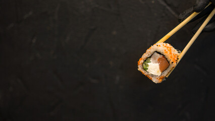 Sushi rolls on a dark background. The hand holds the roll. Sushi sticks