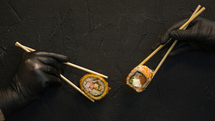 Sushi rolls on a dark background. The hand holds the roll. Sushi sticks