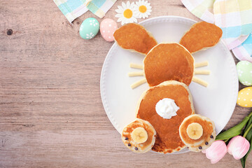 Obraz na płótnie Canvas Cute Easter Bunny pancakes on a white plate. Above view table scene over a wood background.