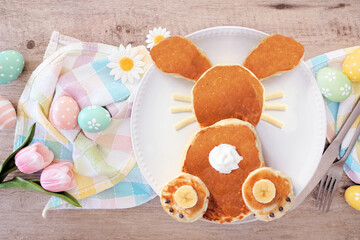 Fun Easter Bunny pancakes on a white plate. Overhead view table scene with Easter eggs on a wood...