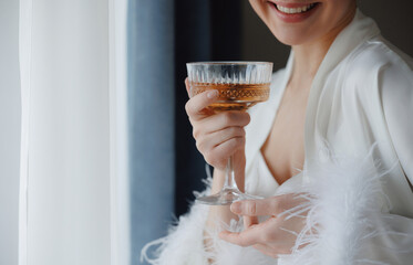 Happy young woman bride with champagne celebrating wedding day, morning