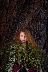 Portrait of a girl with red hair with a bouquet of mistletoe against the background of the textured bark of an old tree.