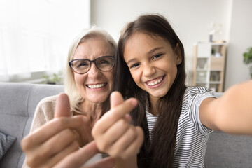 Cheerful senior granny and adorable grandkid girl making little hearts gestures, joining fingers,...