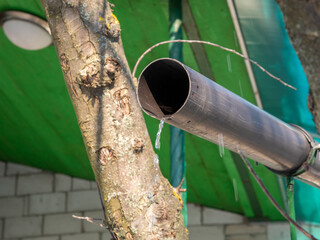 Water flows through metal pipe from roof of house in spring