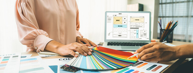 Cropped image of interior designer chooses color from color swatches while laptop displayed website...