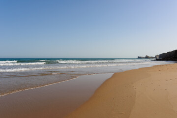 Playa desierta con cielo azul y arena mojada.