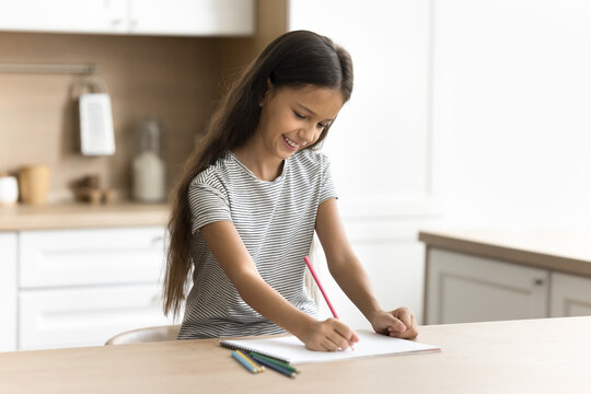 Cheerful little artist kid drawing funny picture in colorful pencils in paper album. Art school pupil girl preparing homework task at home, enjoying creativity, inspiration, leisure, hobby at home