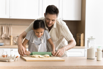 Fototapeta na wymiar Caring young dad teaching preteen daughter in apron to bake in home kitchen. Happy daddy and kid girl preparing homemade fresh bakery meal for family dinner, cooking dessert