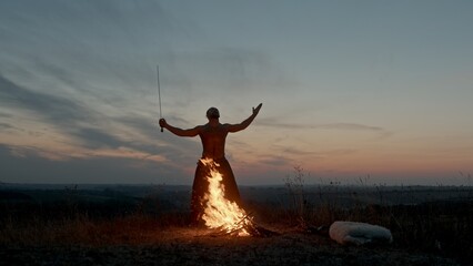 Shirtless warrior praying near fire during sunset - epic powerful shot