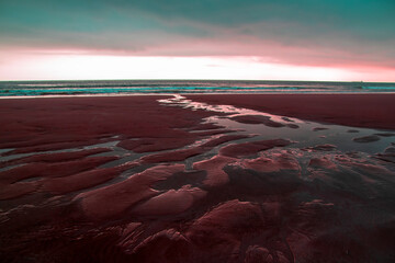 Beautiful sunset at the beach with pink sand and red water.