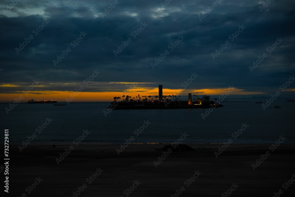 Wall mural Silhouette of an island illuminated by the setting sun against a tranquil, reflective ocean