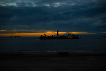 Naklejka premium Silhouette of an island illuminated by the setting sun against a tranquil, reflective ocean