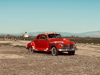 Vintage red car parked in a field, surrounded by tall mountains
