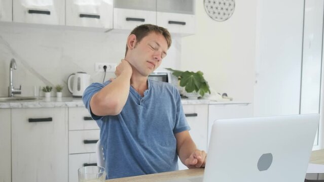 Overworked young businessman suffering from neck pain after had a long day working on laptop at home. Male freelancer have problem with health while working on computer. Office syndrome concept