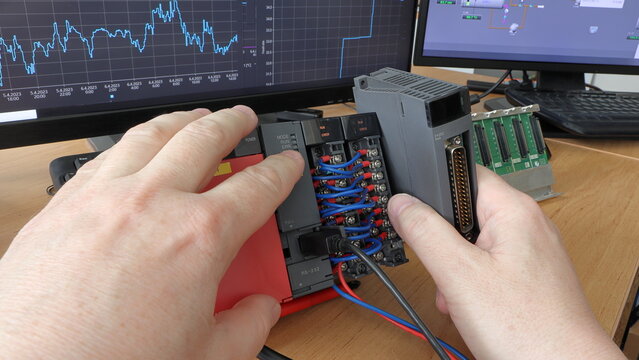 An electrical engineer adds a new IO card to a modular PLC automaton. Programmable logic controller. Trends of measured quantities in the background. Production automation. Automatic control system.