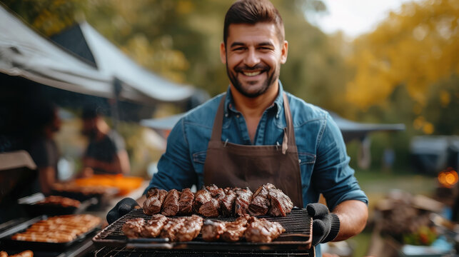 cheerful smiling man in kitchen mittens holds barbecue grill with meat in the park, cook, picnic in nature, cooking, delicious food, meal, summer