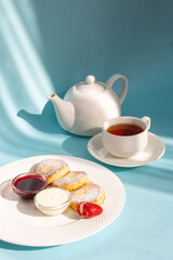 White plate with cottage cheese pancakes, sour cream, jam, and a cup of tea on a blue table.