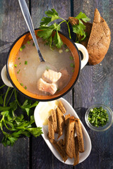 Close-up of a bowl of fish soup with fresh herbs and bread on a wooden table.