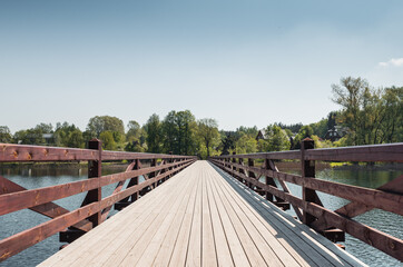 Fototapeta na wymiar Diminishing perspective view of wooden bridge over a lake. Symmetric view of footbridge in countryside on a sunny day
