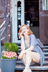 Fototapeta premium Happy smiling red hair woman with glasses speaking by phone outside