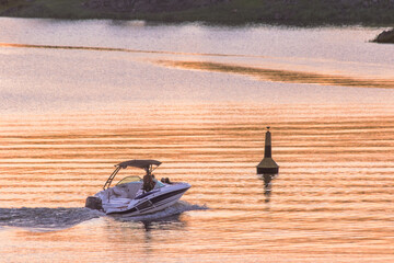 A motor boat navigates the calm waters of the lake during a beautiful summer sunset