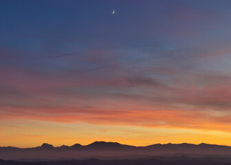 Fototapeta na wymiar Tramonto blu e arancio con luna nel cielo sopra le montagne