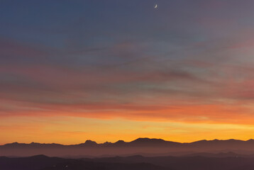 La Luna al tramonto nel cielo arancione sopra le montagne