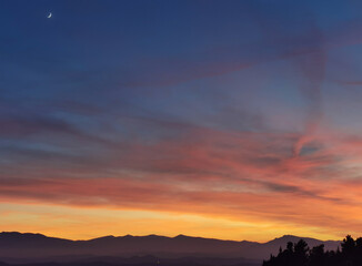 Tramonto blu e arancio con luna nel cielo sopra le montagne