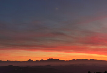 La Luna al tramonto nel cielo arancione sopra le montagne