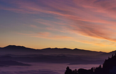 Le valli tra monti si riempiono nel rosso tramonto di un mare di nuvole