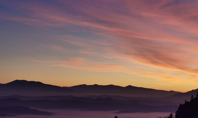 Le valli tra monti si riempiono nel rosso tramonto di un mare di nuvole