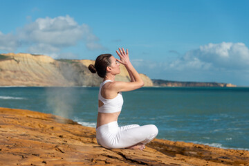 Fototapeta na wymiar sporty woman practicing yoga and meditating on rocks by the sea.