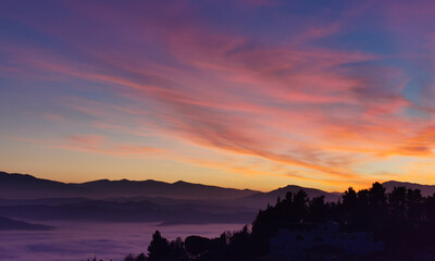 Le valli tra monti si riempiono nel rosso tramonto di un mare di nuvole