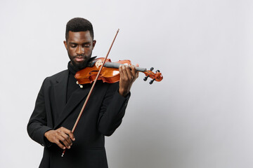 Elegant African American man in tuxedo playing violin against white background in classical music performance concept