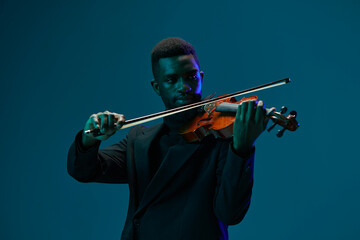 Elegant man in black suit playing the violin against a vibrant blue background in a classic musical...