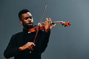 African American man playing violin in black suit on gray background, artistic music performance concept