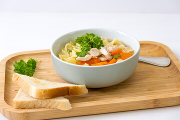 Homemade chicken soup with noodles and vegetables in a white bowl, white background. Healthy warm comfortable food.