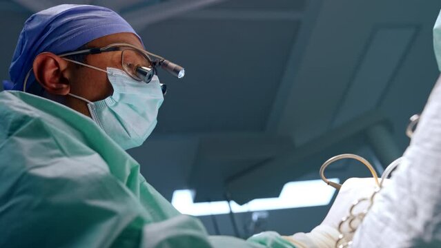 Confident Caucasian surgeon wearing surgical loupes, mask and cap. Low angle portrait of a doctor performing microsurgery.