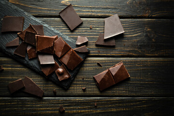 Broken pieces of dark chocolate bar on a black vintage table. View from above