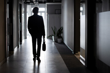 Silhouette of a businessman in full height, a man inside the office walks along the corridor,...