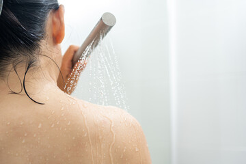 Female in shower rinse shampoo with water dripping on body. Young woman taking shower and washes soap bubbles off her body with water from the shower. Enjoying routine procedure at home.